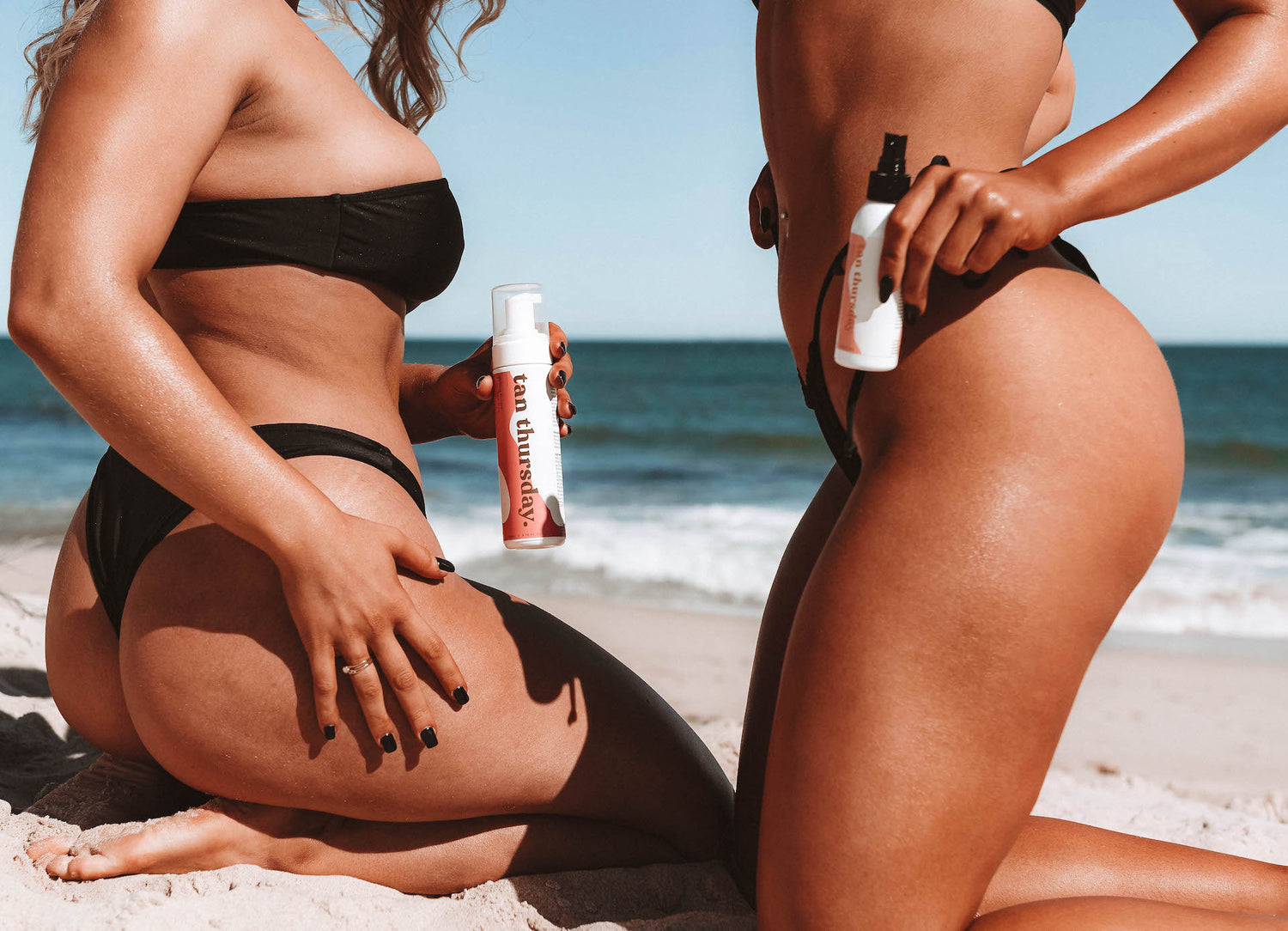 A close up of two women kneeling on a beach, holding Tan Thursday product